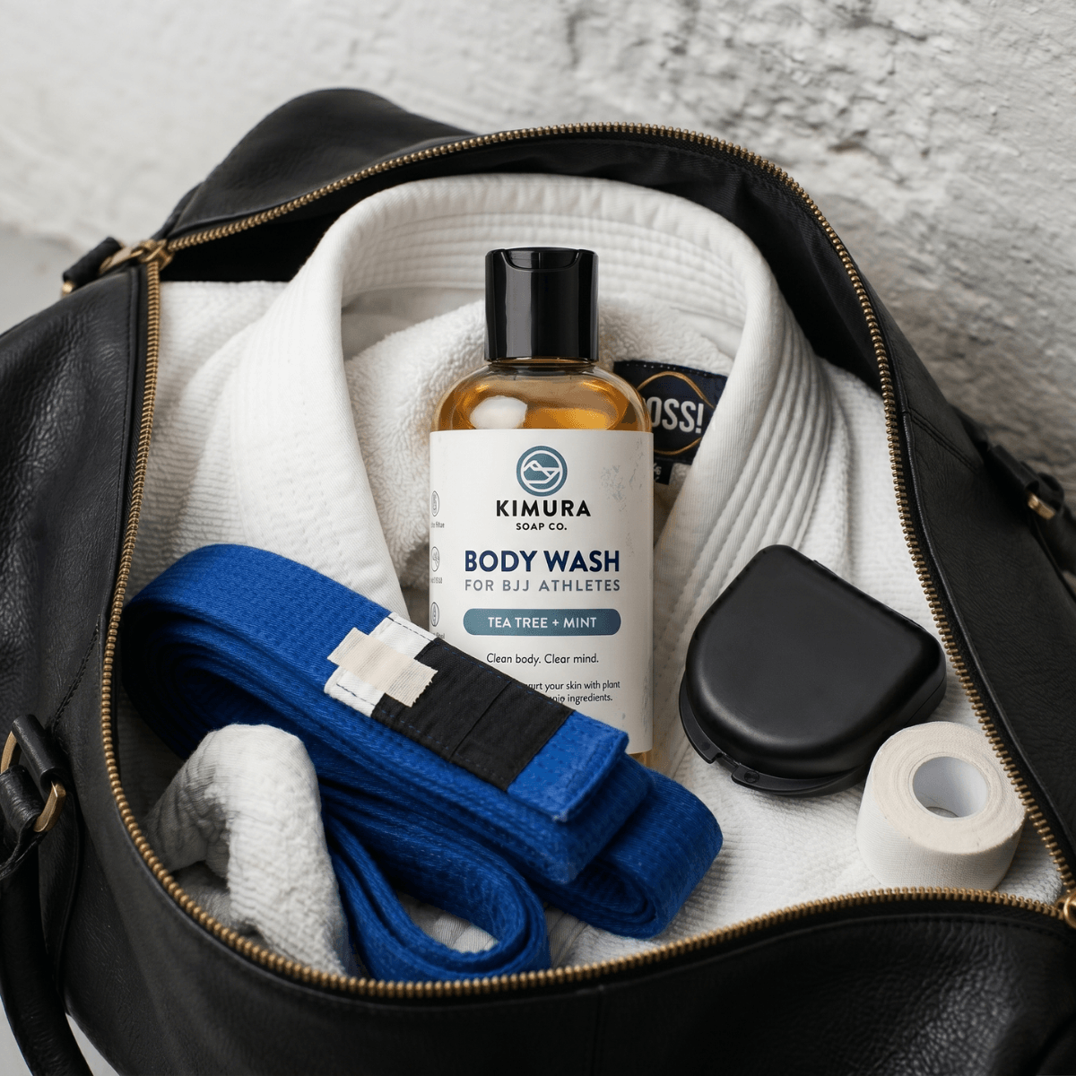 Open black leather bag with Kimura Soap Co body wash, towel, and other items.