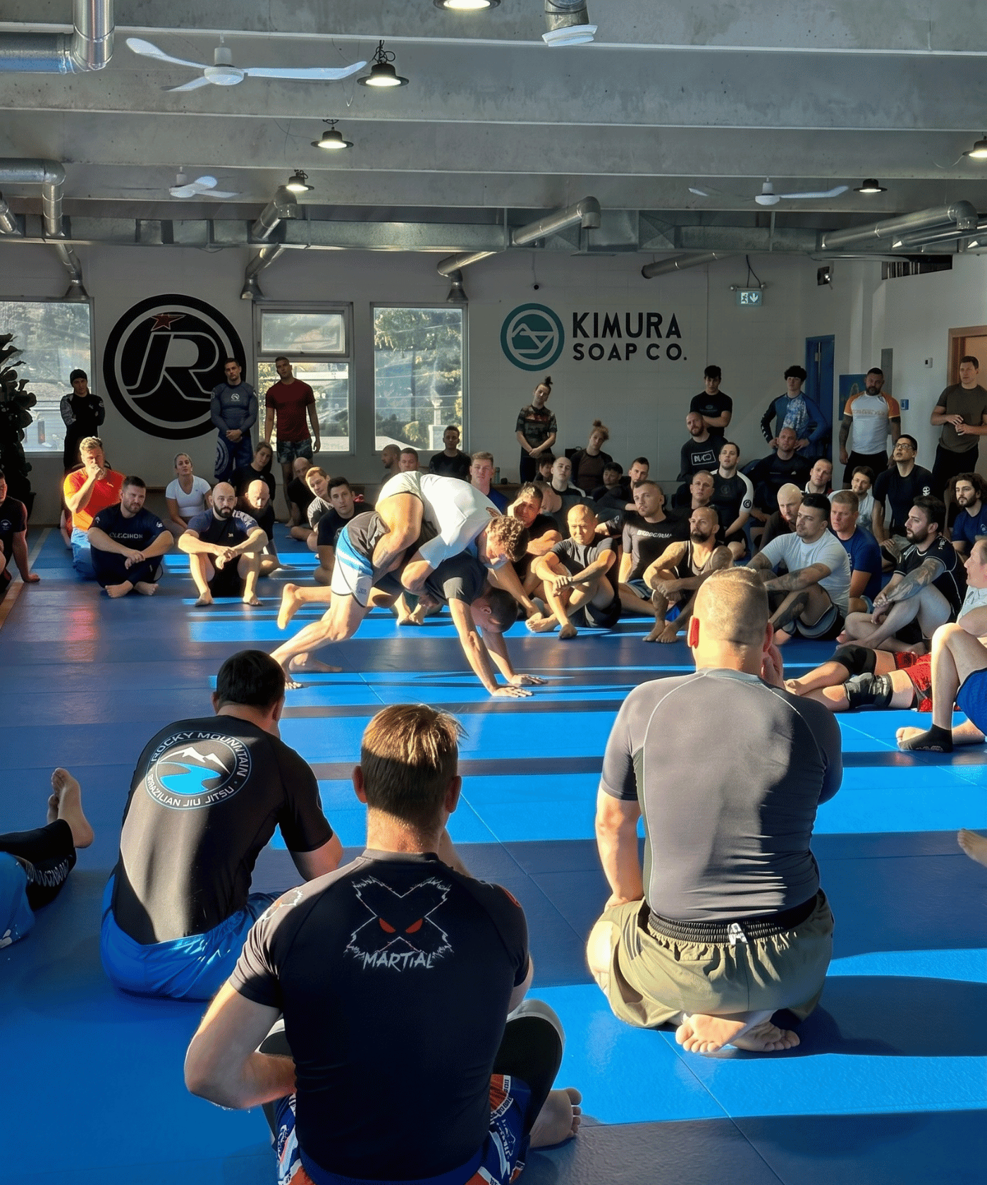 Group of people practicing bjj in a gym with 'Kimura Soap Co' branding.