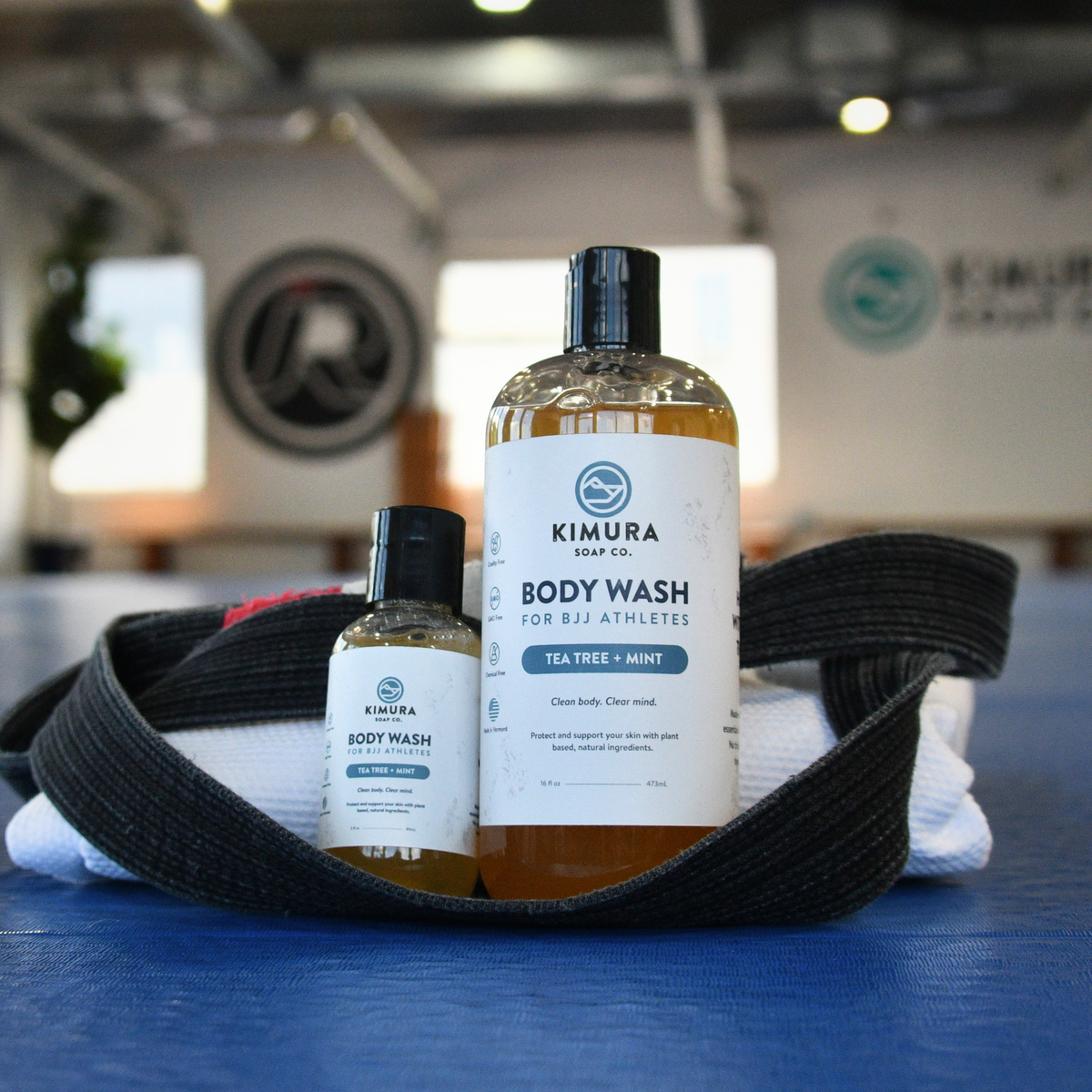 Two bottles of Kimura Soap Co. body wash on a blue mat with a black belt and towel in the background.