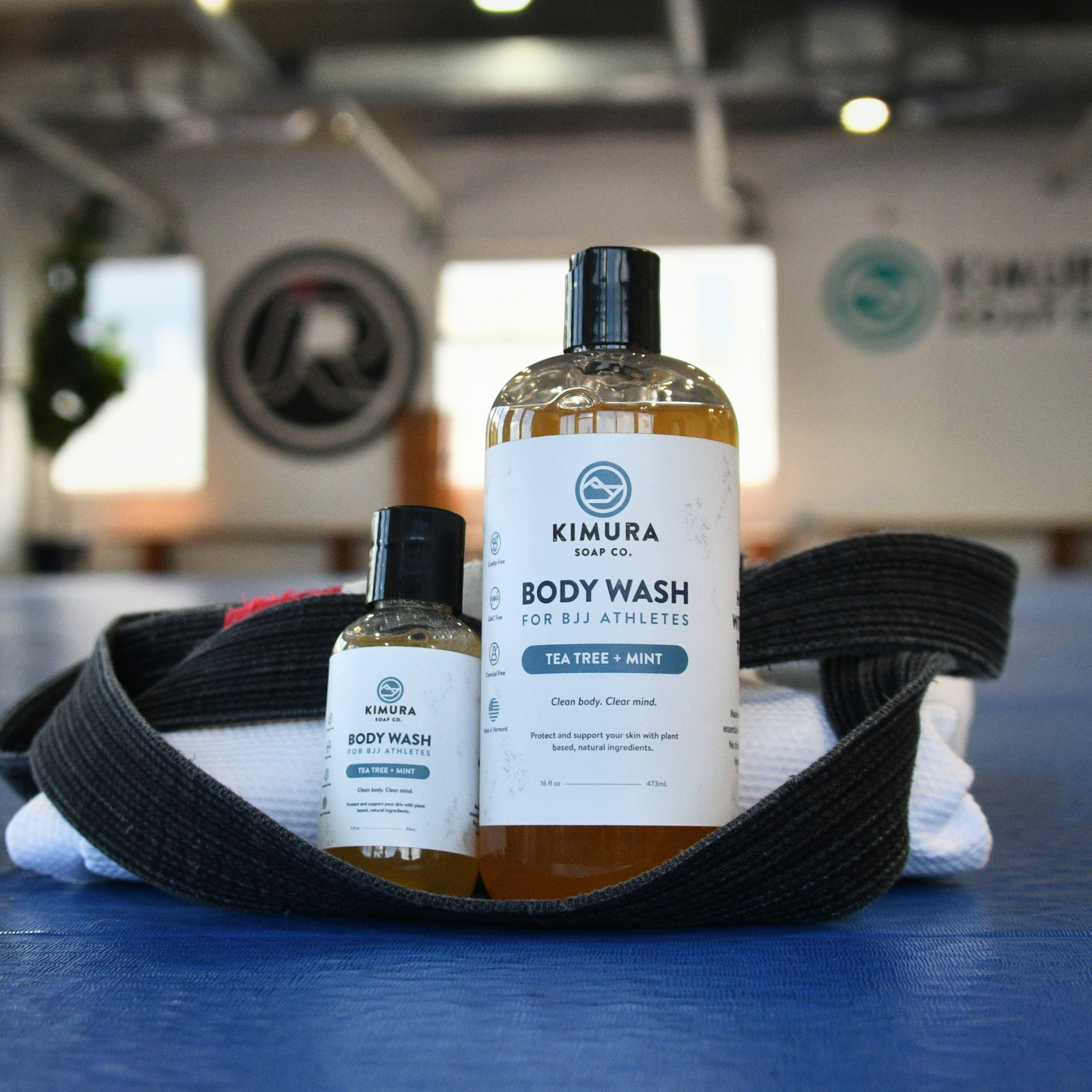 Two bottles of Kimura Soap Co. body wash on a blue mat with a black belt and towel in the background.